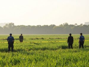 Investigative scene in a field near a home with police tape.