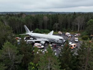 Aerial view of a plane crash site in Maine with emergency services responding.