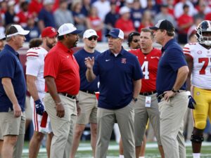 A diverse group of college football coaches discussing strategy on the sidelines.